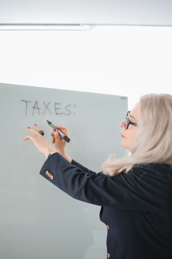 Businesswoman in glasses writing taxes on the whiteboard in a professional setting.